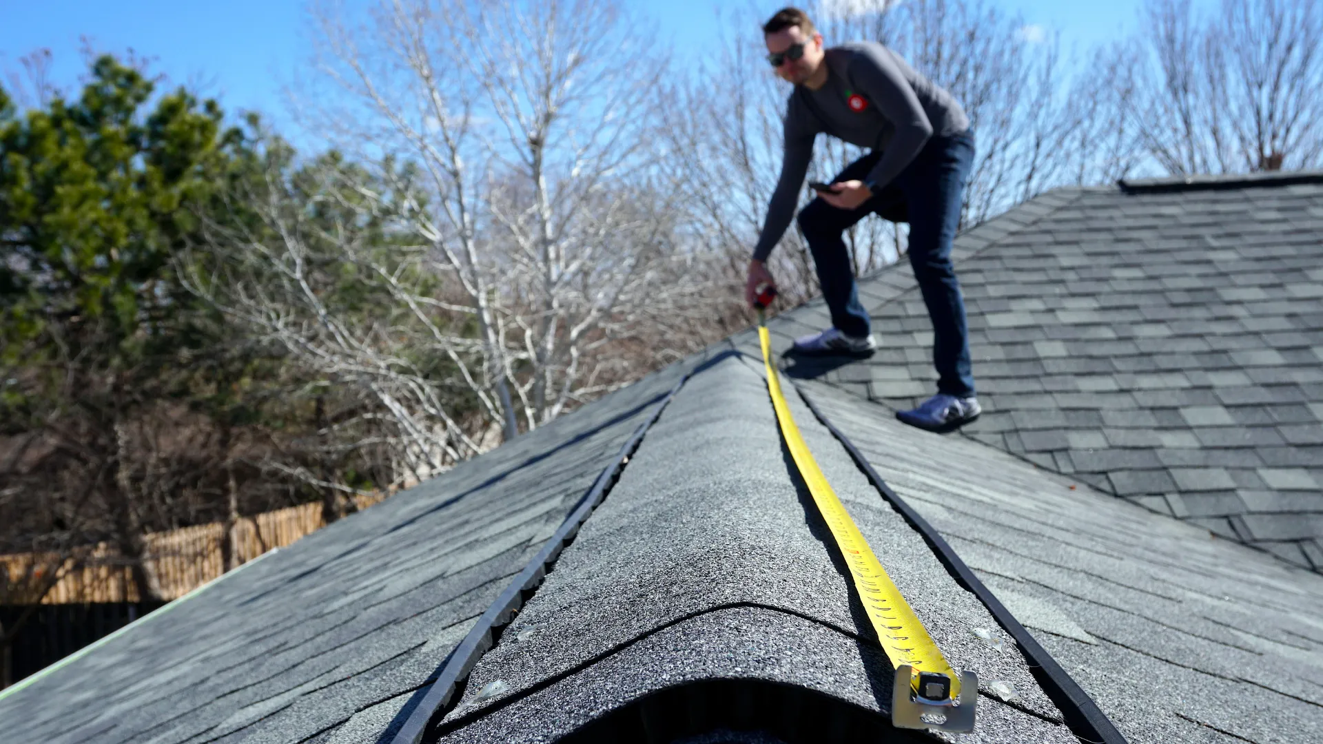 Roofer measuring a shingle roof with a tape measure