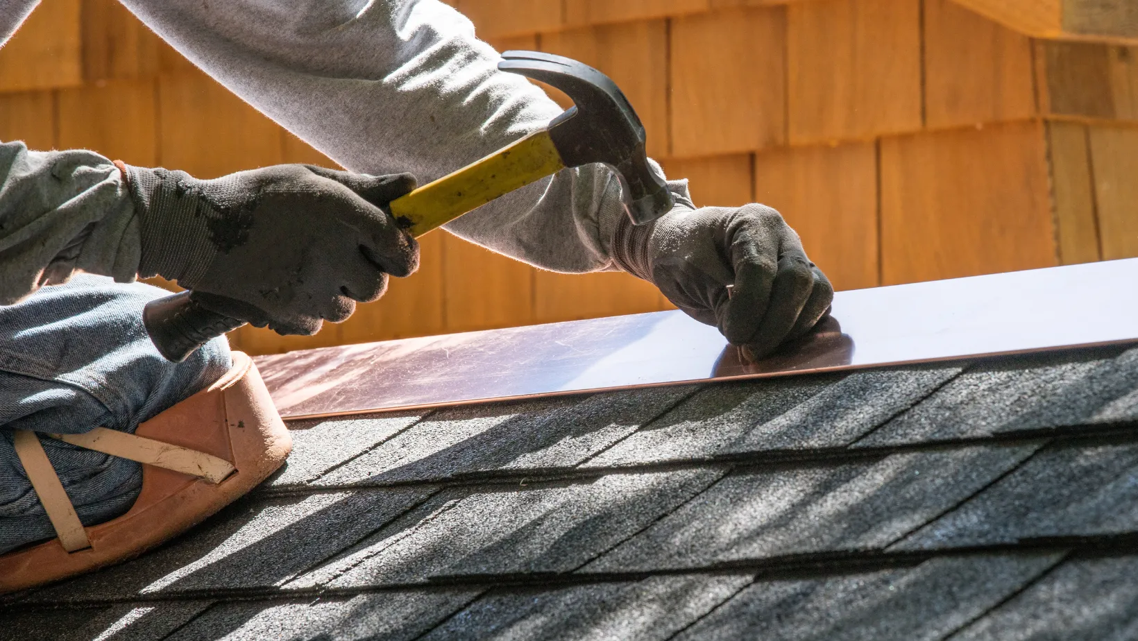Roofer hammering metal flashing onto asphalt shingles