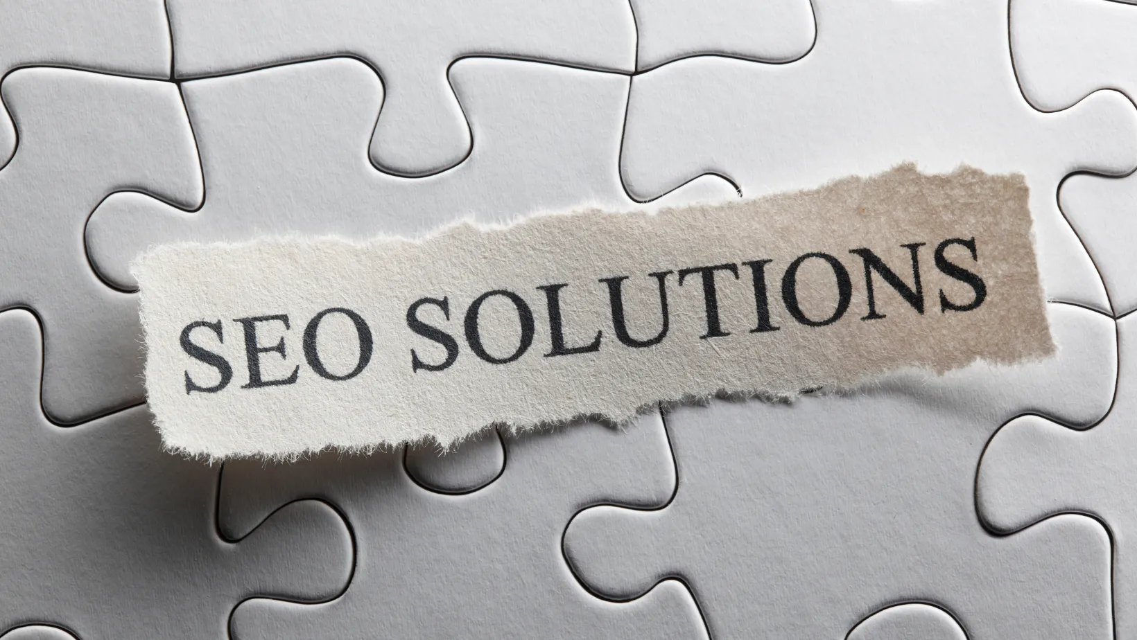 Torn paper reading SEO SOLUTIONS on white puzzle pieces