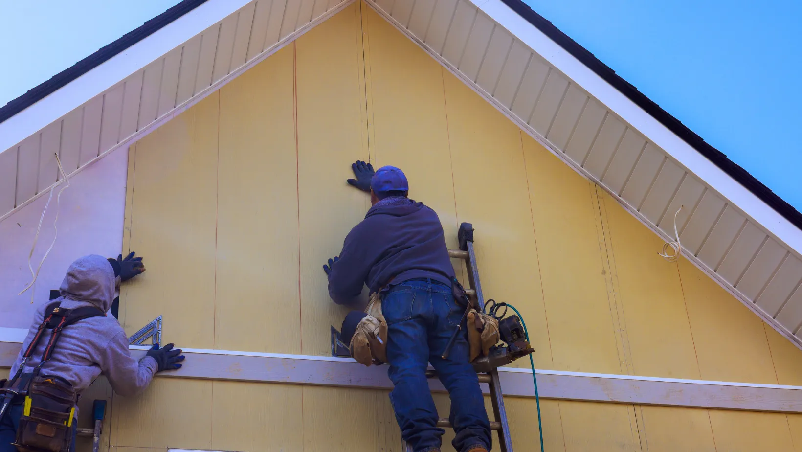 Two installers fitting siding panels on a house gable